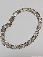 Top view of the sterling silver bracelet showing the entire length laid in a loop, emphasizing the woven braided design and lobster claw clasp.