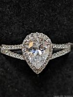 Close-up front view of pear-shaped cubic zirconia center stone with halo setting on sterling silver band.