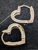 Pair of heart-shaped sterling silver earrings shown flat, displaying front and back with minor tarnish.