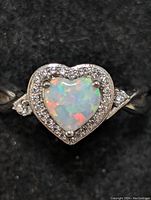 Close-up front view of heart-shaped opal ring with surrounding cubic zirconia and silver band on black background