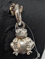 Close-up front and side views of the sterling silver frog pendant, showing detailed craftsmanship and eye stones.