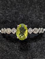 Close-up front view of sterling silver ring with an oval peridot gemstone and small clear stones on the band