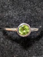 Close-up front view of sterling silver ring with round green faceted peridot gemstone set in bezel.