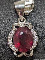 Close-up of the sterling silver pendant showing oval ruby gemstone at center with clear stones surrounding it