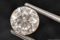 Close-up image of the round brilliant cut moissanite gemstone held by tweezers showing the facets and clarity from the top view.