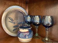Photo displaying ceramic vase, three blue wine glasses, and decorative plate.