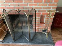 Brass three-panel fireplace screen with mesh placed in front of a brick fireplace.