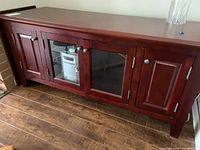 Front view of wooden cabinet with built-in silver CD player visible through glass paneled doors and solid wood doors on sides, standing on wooden floor.