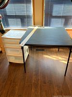 Side view of black folding table next to white plastic storage drawers