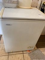 Front view of white Danby deep freezer showing brand label and power control dial, placed on tiled floor.