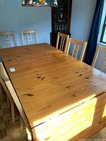 Solid pine rectangular dining table with six chairs around it, showing natural wood grain and light wear.