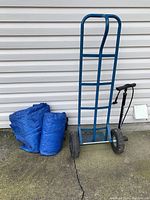 Photo of blue dolly with two tires, two rolled blue tarps, and black bike pump outside against a wall.