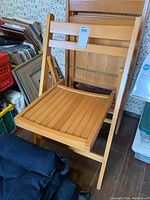 Front view of one wooden folding chair showing slatted wooden seat and backrest with cushions in front.