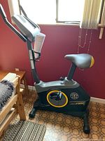 Side view of Gold's Gym stationary bike model 200C positioned indoors near a window, showing entire bike with seat, pedals, and digital console.
