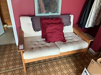 Image showing cream tufted loveseat with wooden frame, red throw pillows, and portion of framed wall art above