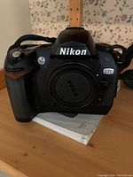 Nikon D70 camera front view showing brand name and model number, body cap installed, camera strap attached.