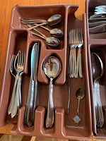 Brown plastic flatware organizer tray containing multiple pieces of Oneida Oneidacraft Deluxe stainless steel flatware, including teaspoons, knives, forks, and a small sugar spoon.