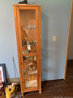 Front view of tall pine display cabinet with glass door showing interior shelves and collectibles inside.