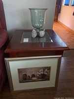 Overall view of wooden side table with glass decor on top and framed print leaning against it