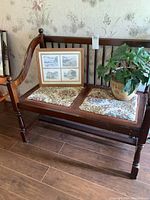 Front view of vintage wooden bench with needlepoint seating cushions, with picture frame and potted plant on seat.