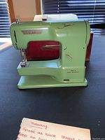 Front left view of green Elna Junior sewing machine with threading instructions card visible