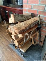 Vintage wood holder stand holding several pieces of firewood, showing rustic metal arms and base.