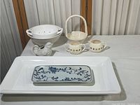 Wide shot showing collection of white ceramic items including platter, blue and white plate, bird cream dish, colander, basket dish, cream and sugar set