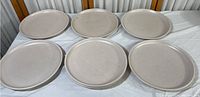 Six beige speckled ceramic vintage dinner plates arranged flat on a white surface, showing full set and size consistency.