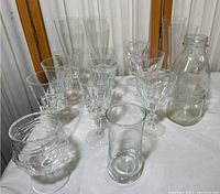 Full collection of clear cocktail glasses displayed together on a white cloth, including various stems and a glass bottle.