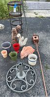 Full view of garden accessories collection on asphalt showing umbrella holder, terra-cotta rabbit, four-level stand, assorted planters and decor items