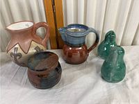 Five-piece pottery kitchen set displayed on a table showing all items together including two pitchers, one jar, and two green pear-shaped shakers.