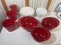 Photo showing collection of three large red plastic mixing bowls with spouts and handles, three red plastic planters, and three white ceramic mixing bowls.
