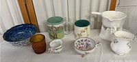 Collection of assorted porcelain and china items including bowls, mugs, creamers, and a glass.