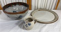 Photo showing the three pottery items: a large bowl with a bird motif, a large beige plate, and a small jug with blue designs.