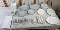 Full display of all white/off-white dinnerware pieces on a table including platters, bowls, egg holder, plates, and serving pieces.
