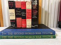 Books standing upright showing spines and titles, some dust jackets worn and damaged.