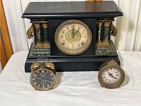 Overview of three clocks on white surface: large wooden mantel clock at back, two smaller clocks in front