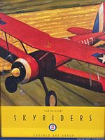 Close-up photo of the colorful poster showing a red biplane with star insignias and the Skyriders title, signed by Karen Dupre.