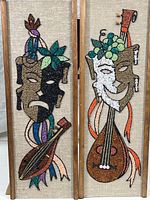 Full view of the two wall hanging panels side by side, showing the comedy and tragedy masks, musical instruments, and decorative elements in colored glass chips and gold mosaic tiles on a fabric background and wood frames.