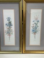 Pair of gold framed floral watercolor prints, vertically oriented, showing full artwork and frames.
