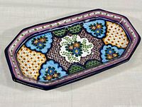 Full top view of hand painted ceramic serving dish showing colorful floral and geometric patterns with purple border.