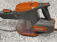 Close-up of the vacuum main body showing the dust container, handle, power button, and Shark Rocket branding in orange and dark gray colors.