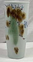 Full view of tall cylindrical white ceramic vase with botanical hand painted design and blue Chinese characters.