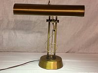 Full view of vintage brass piano sheet music lamp with elongated fluorescent tube and supportive base on a neutral background.