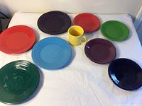 Top view of 8 Fiesta plates in various colors and 1 yellow mug.