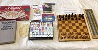 Photo of the entire lot showing chess board with chess pieces, polymer dominoes, Scrabble game box, Players Dictionary, cribbage board, dice, colored pencils, and Mexican Train instructions.