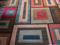 Close-up of the geometric pattern on the rug showing rectangles and squares in red, brown, beige, olive, teal, and sage colors.