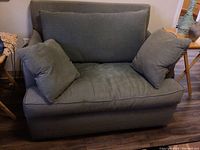 Front view of oversized sage green fabric armchair with two matching pillows on seat.