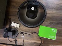 Top view of Roomba showing CLEAN button, power base charger with adapter, extra brushes, and owner's manual.