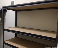 Photo showing the middle shelves of the shelving unit against a wall, highlighting pressed wood surfaces and black steel frame.